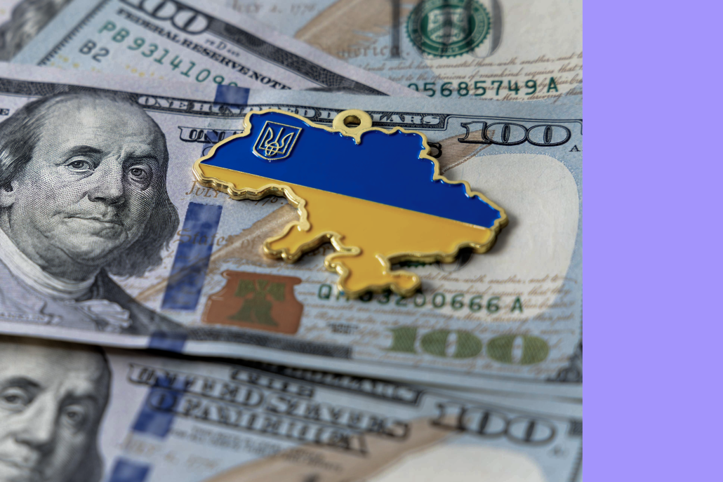 A metallic Ukraine-shaped pin in national colours placed on US dollar banknotes, symbolising financial support to Ukraine.